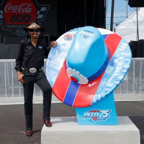 Seven-time NASCAR Cup Series champion Richard Petty poses next to his Petty hat statue in front of Charlotte Motor Speedway. 